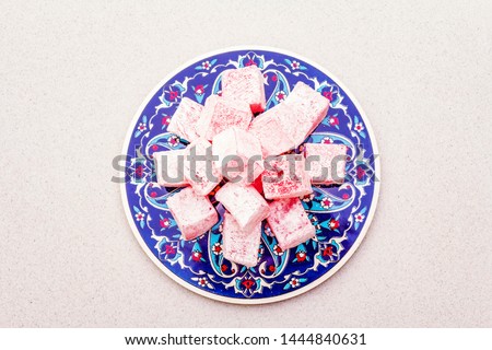 Eastern sweets. Traditional Turkish delight Rahat lukum with a rose on ceramics with typical folk patterns. Stone background, copy space, top view Royalty-Free Stock Photo #1444840631