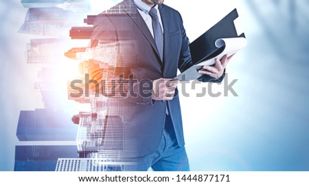 Unrecognizable young businessman holding clipboard standing over blue background with double exposure of cityscape. Concept of leadership. Toned image mock up