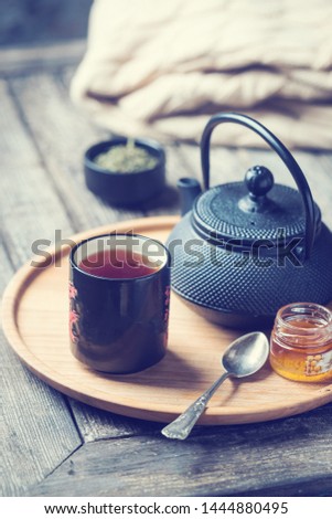 Still life of black tea cup with tea pot on a tray over wooden table. Tea time in a cozy atmosphere