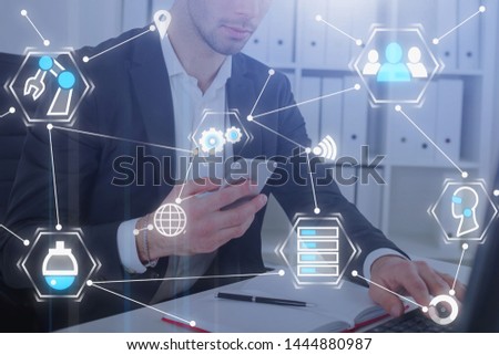 Businessman working with phone and laptop in office with double exposure of business interface. Concept of hi tech. Toned image