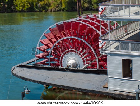 Red Riverboat Paddle Wheel in a River with Trees Royalty-Free Stock Photo #144490606