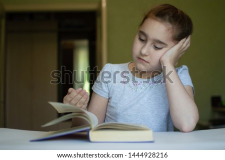 tortured girl child reads a book at the table and she is very tired and wants to sleep, yawns, falls asleep while reading stories and lessons