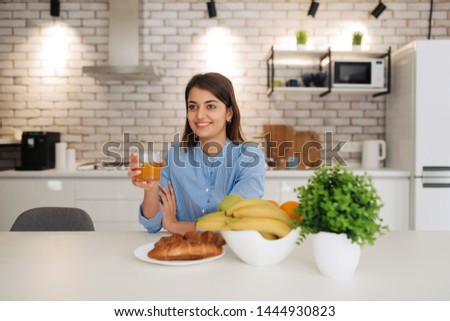 Smiling woman eating healthy food while sitting and having breakfast at the kitchen table.
