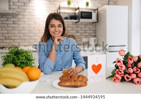 Happy mother's day! Attractive woman with flowers and postcard sitting on kitchen. Family holiday.