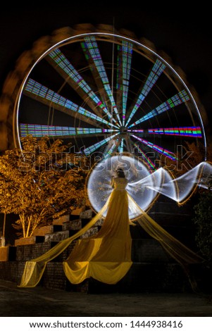 Beautiful Indonesian female wearing yellow long was standing alone decorated with a white circle light painting as a backdrop on the site area of ​​a night tour