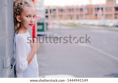 fashionable and happy teen girl posing next to the building and lattice