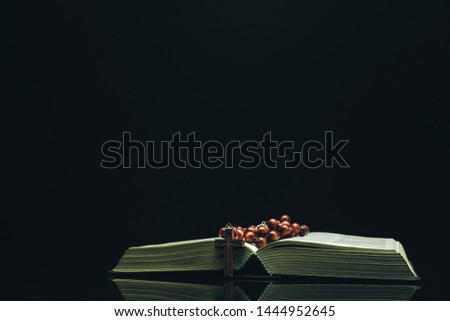 Open Holy Bible and beads on a black glass table dark background