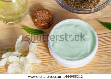 Jar of cream made from natural plant ingredients, oils and herbs, jasmine flowers on a light wooden background - preparation of organic cosmetics concept, close up