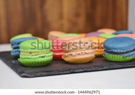 Different types of sweet different colored macarons pastry on a black stone plate at a banquet on wooden background