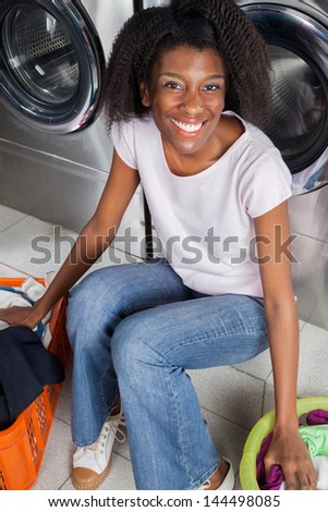 Portrait of young African American woman with clothes baskets sitting in laundry