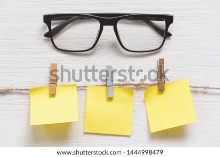 Blank paper stickers with copy space on a clothespin on a rope and eye glasses on a white table background. To do list.