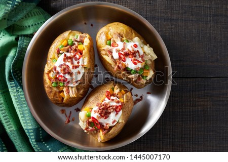 Oven baked potatoes stuffed with chicken meat, bacon, cheddar, sour cream, green peas, served on a metal skillet sprinkled with caramelized bacon, red chili, view from above, copy space Royalty-Free Stock Photo #1445007170