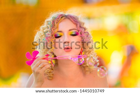 Emotions of happiness and fun. Beautiful young happy girl with a colorful summer rainbow makeup inflates soap bubbles. Summer holidays, playful mood at a party, amusing soap bubbles.