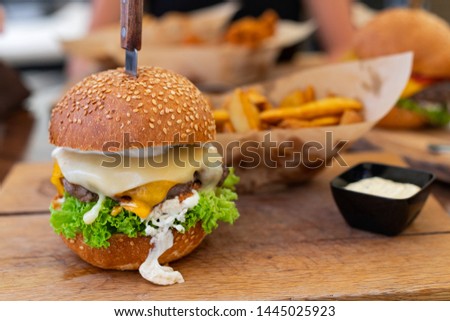 Picture of a delicious juicy cheeseburger served with wedges and tartar sauce on wooden plate