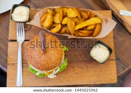 Picture of a delicious juicy cheeseburger served with wedges and tartar sauce on wooden plate