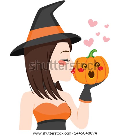 Beautiful young brunette witch kissing pumpkin on Halloween