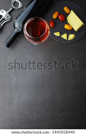 Red wine on a stone background. Wine glass and black wine bottle. Nuts cheese and tomatoes for snack.