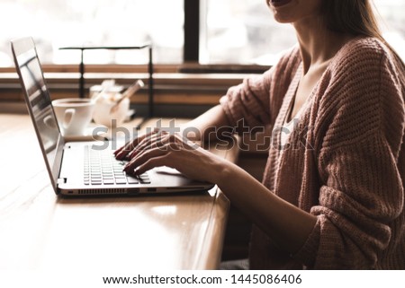 Attractive young woman sits at a table in a cafe with a cup of coffee and enjoys a laptop