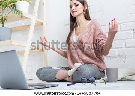 A young happy woman sits on the floor in a yoga apartment in a bright apartment and works at a laptop, a freelancer girl meditates while then the job stresses out