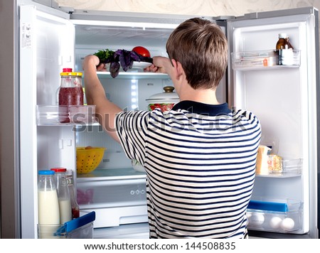Attractive man looking for something in the fridge at home. Hungry young man opens the refrigerator. The food in the refrigerator. Royalty-Free Stock Photo #144508835