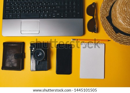 accessories for work with travel on the beach: laptop, wallet, straw hat, notepad, telephone, vintage camera, pen, sunglasses on a yellow background top view.