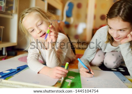 Two cute little sisters writing letters together at home. Older sister helping youngster with her homework. Education for kids.
