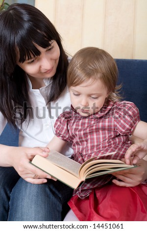 Mother reading a book with her little daughter on sofa at home