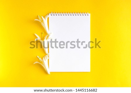 A notebook decorated with white flowers and lilies of the text. White flowers with open Notepad on yellow background, top view, flat lay.
