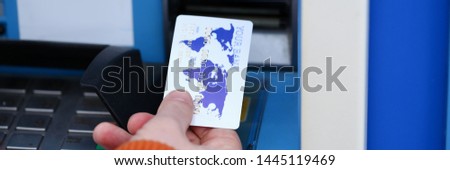 Male hand hold white credit card aganist ATM background.