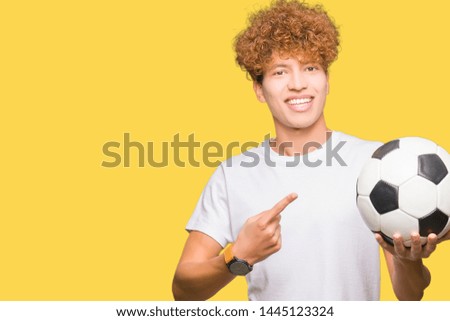 Young handsome man holding soccer football ball very happy pointing with hand and finger