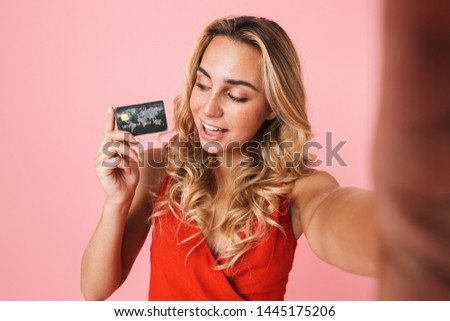 Lovely young blonde woman wearing summer dress standing isolated over pink background, taking a selfie, showing plastic credit card