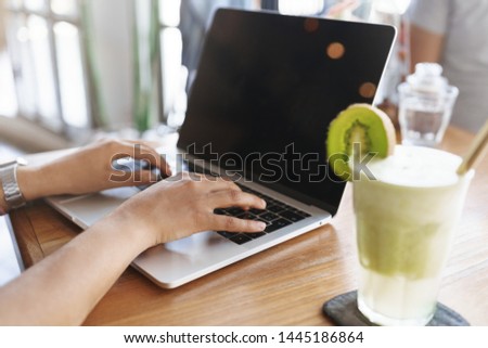Cropped shot woman hands typing laptop keyboard blank screen, sitting indoor cafe table drink green smoothie cocktail prepare university exam working outside office freelancing, digital nomad concept
