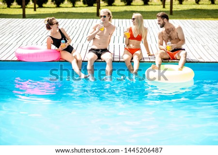 Group of happy friends sitting with inflatable toys on the poolside in a row, enjoying summer time on the swimming pool