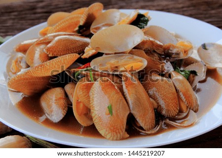 Stir fried clam with chili paste and thai basil leaf in white dish,On the wooden, This is thai food cuisine.