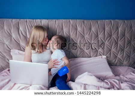 Mother and son having fun while sitting with laptop on bed