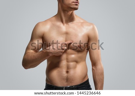 Anonymous shirtless athlete pointing at pectoral muscle after workout against gray background Royalty-Free Stock Photo #1445236646