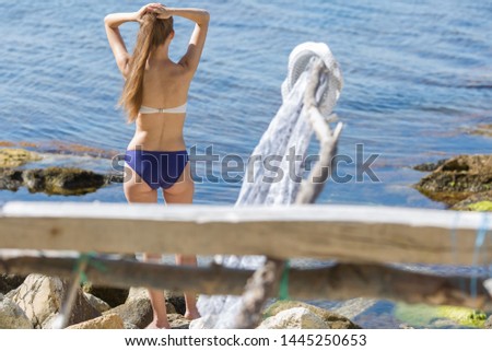 Rear view of long-haired girl in swimsuit. Young woman posing with hands behind head on seashore