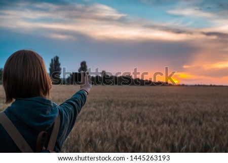 A woman takes a photo of a sunset on a wheat field.