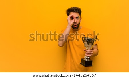 Young man holding a trophy making the gesture of a spyglass