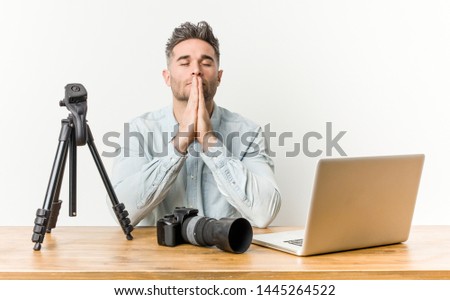 Young handsome photography teacher holding hands in pray near mouth, feels confident.