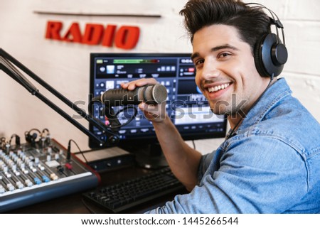 Handsome happy young male radio host broadcasting in studio, using microphone and headphones