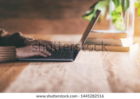 Closeup image of hands using and typing on laptop computer keyboard on wooden table