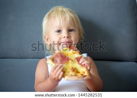 Cute little Caucasian kid eating pizza. Hungry child taking a bite from pizza on a pizza party. Smeared toddler