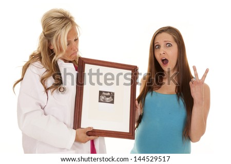 A pregnant woman with a shocked expression on her face holding up two fingers for twins.