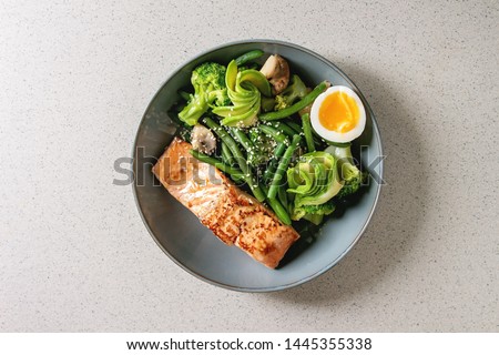 Ketogenic low carb diet dinner grilled salmon, avocado, broccoli, green bean and soft boiled egg in ceramic bowl over grey spotted background. Flat lay, space Royalty-Free Stock Photo #1445355338