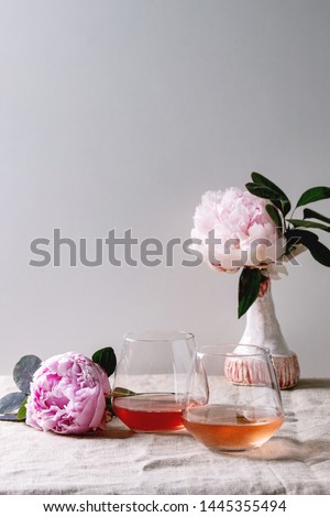 Two glasses of different rose wine standing on grey linen table cloth with pink peonies flowers. Romantic greeting card. Copy space