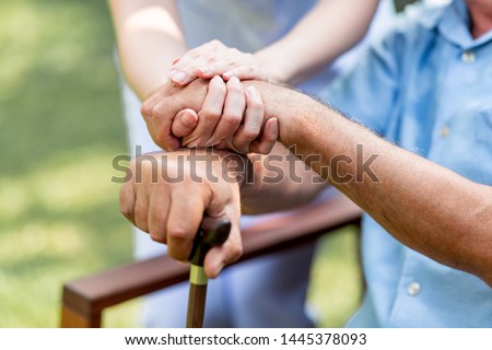 Caring nurse helping senior man sitting on bench in gaden. Asian woman, caucasian man. Holding hands with cane, close up. Royalty-Free Stock Photo #1445378093