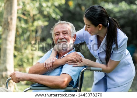 Caring nurse with senior man sitting on wheelchair in gaden. Asian woman, caucasian man. Happy feeling. Royalty-Free Stock Photo #1445378270