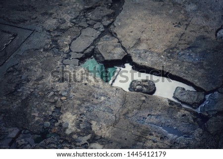 Potholes in old pavement full of shinny rain water Royalty-Free Stock Photo #1445412179