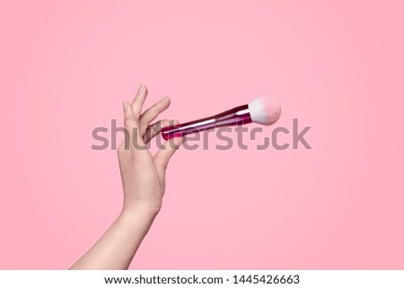 Hand of anonymous female model showing soft clean brush for cosmetics application against pink background